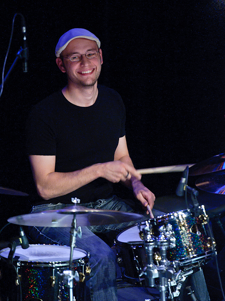 Le batteur jouant derrière sa batterie avec un grand sourire
